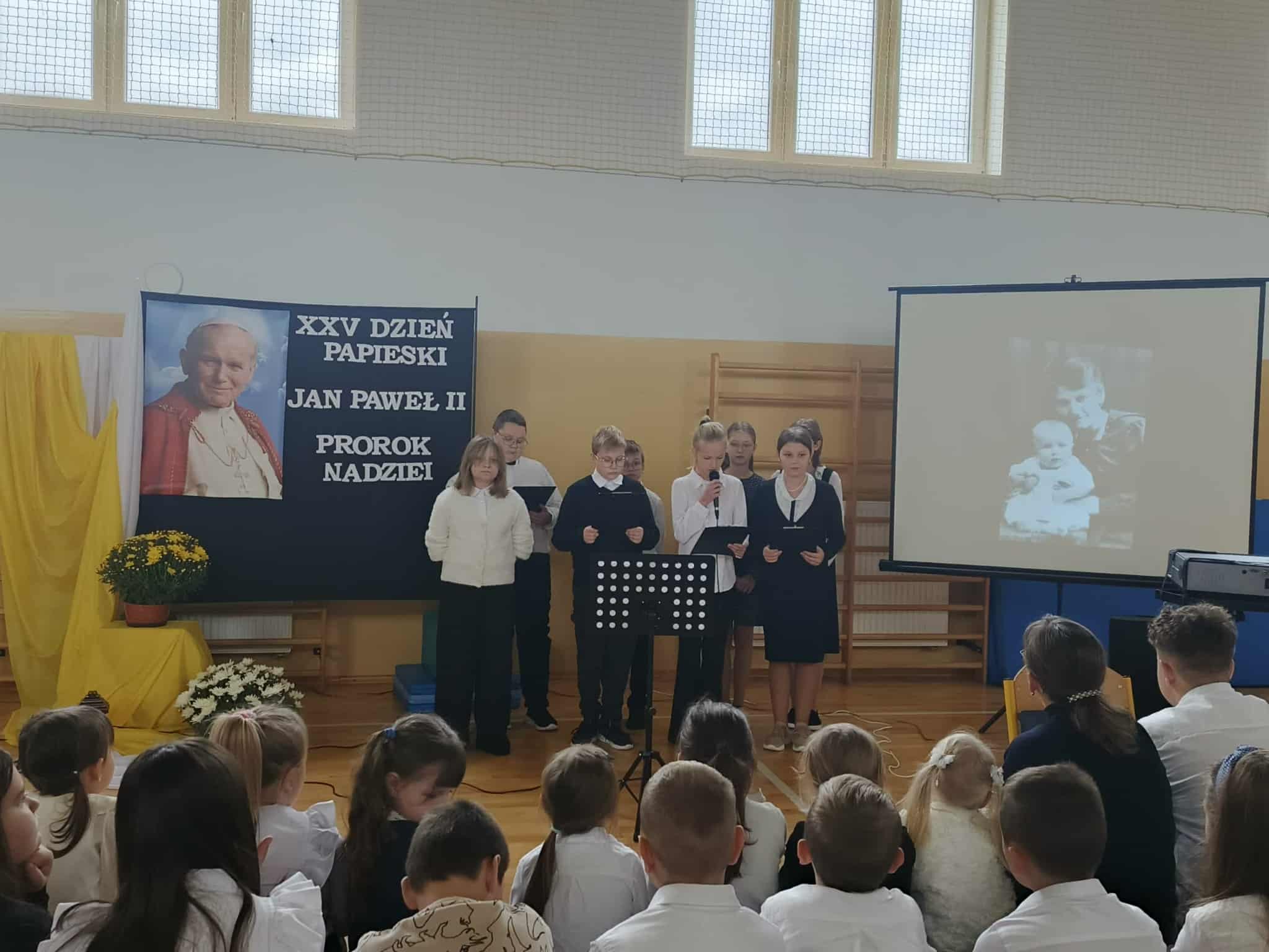 Grupa uczniów śpiewa pieśń podczas szkolnych obchodów XXV Dnia Papieskiego.