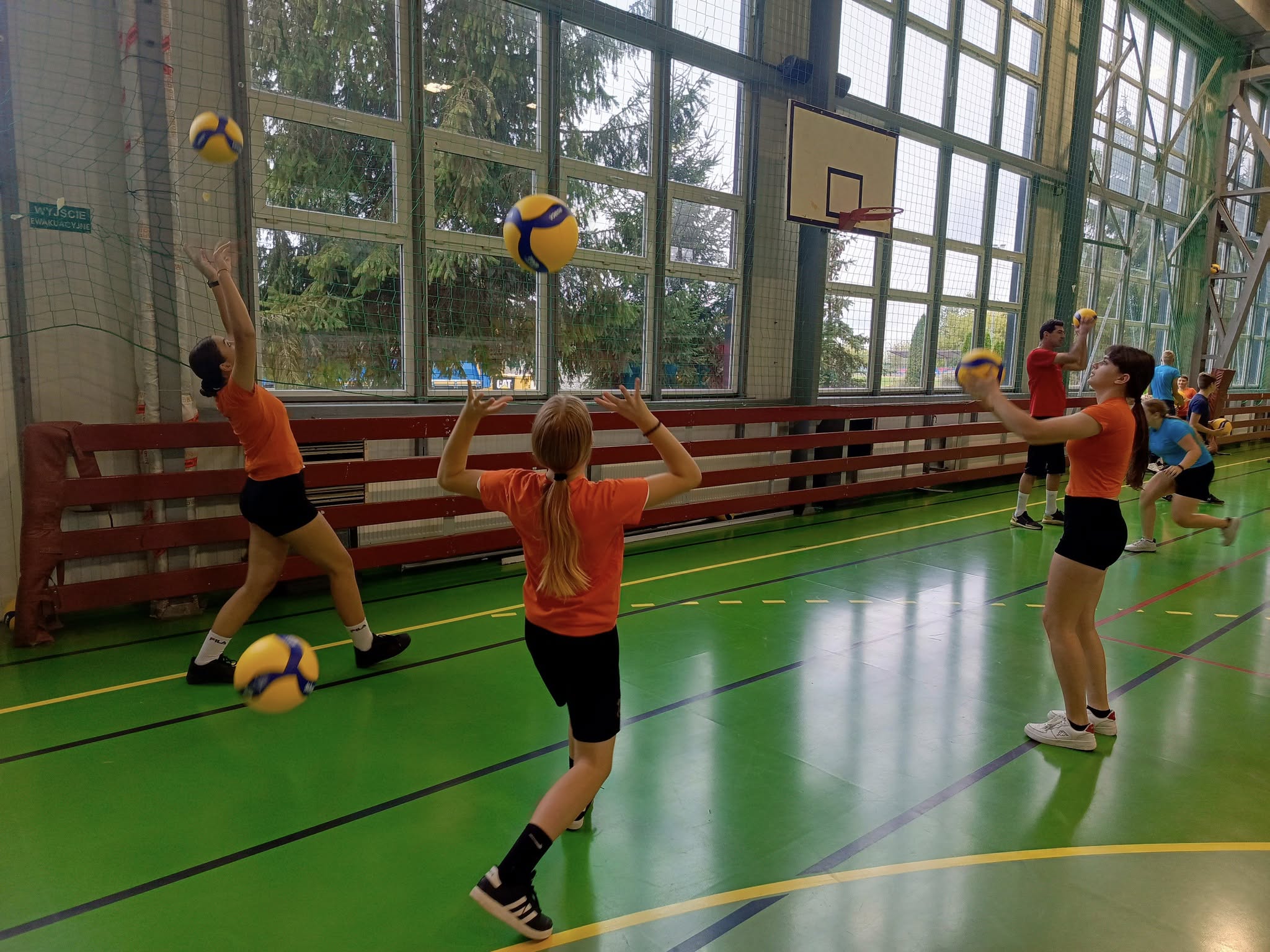 Trzy uczennice w strojach sportowych odbijają piłki