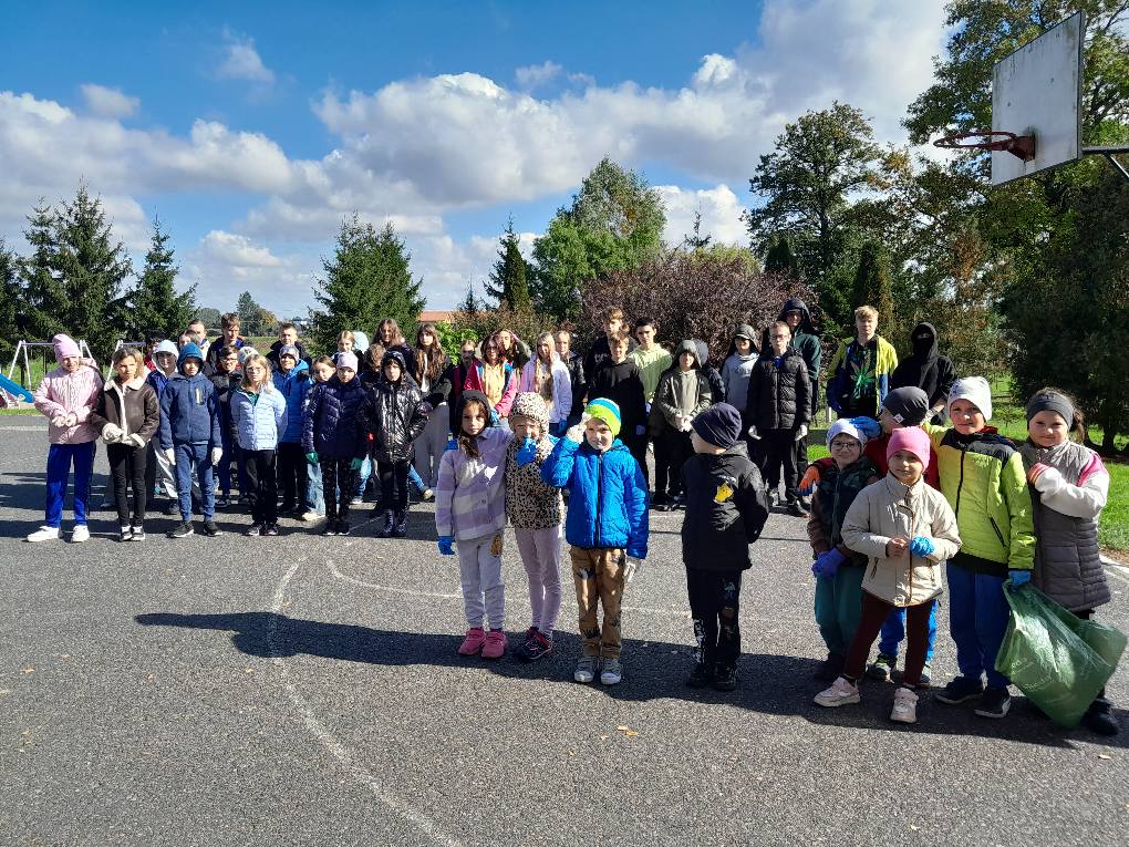 Uczniowie zgromadzeni na boisku szkolnym, trzymają worki pełne śmieci