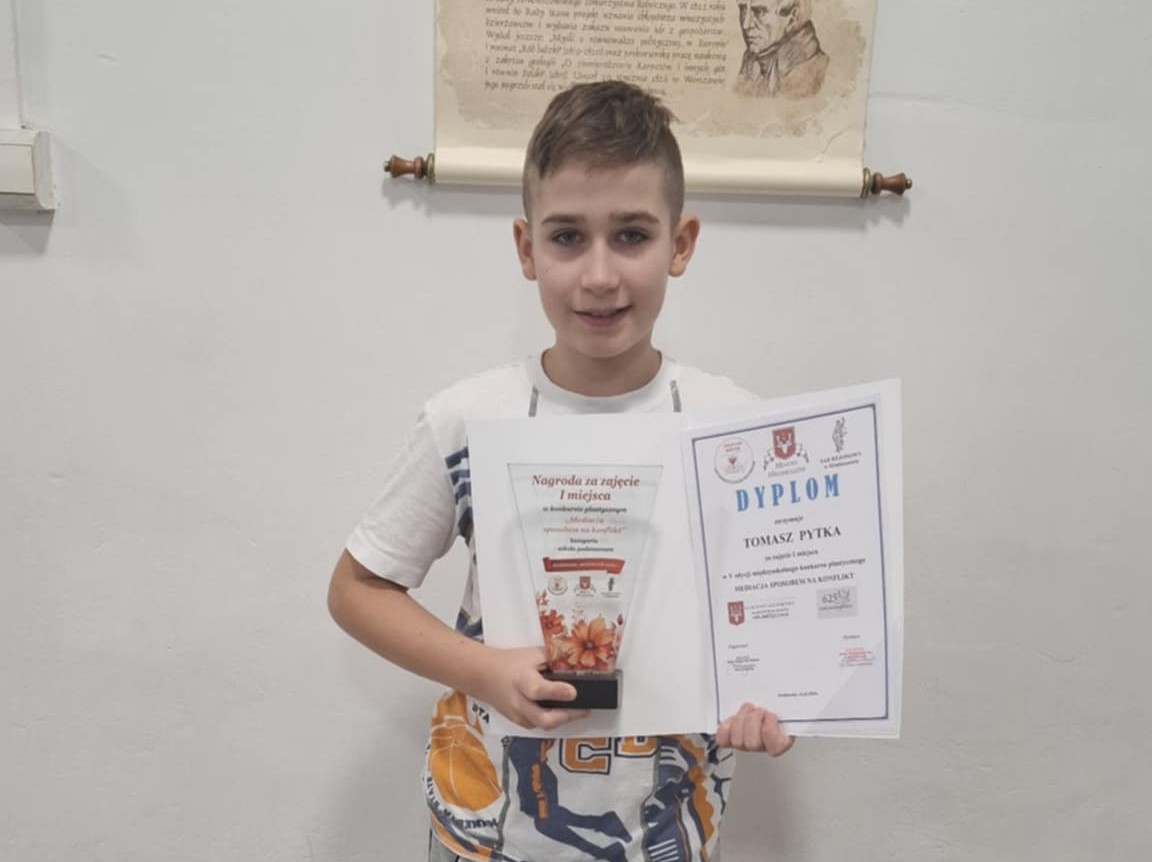 Uczeń klasy piątej trzyma w dłoniach dyplom i pamiątkową statuetkę