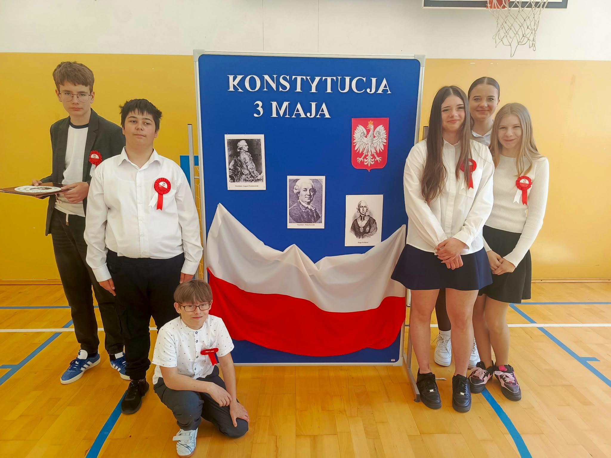 Uczniowie występujący na uroczystym apelu przed tablicą dekoracyjną