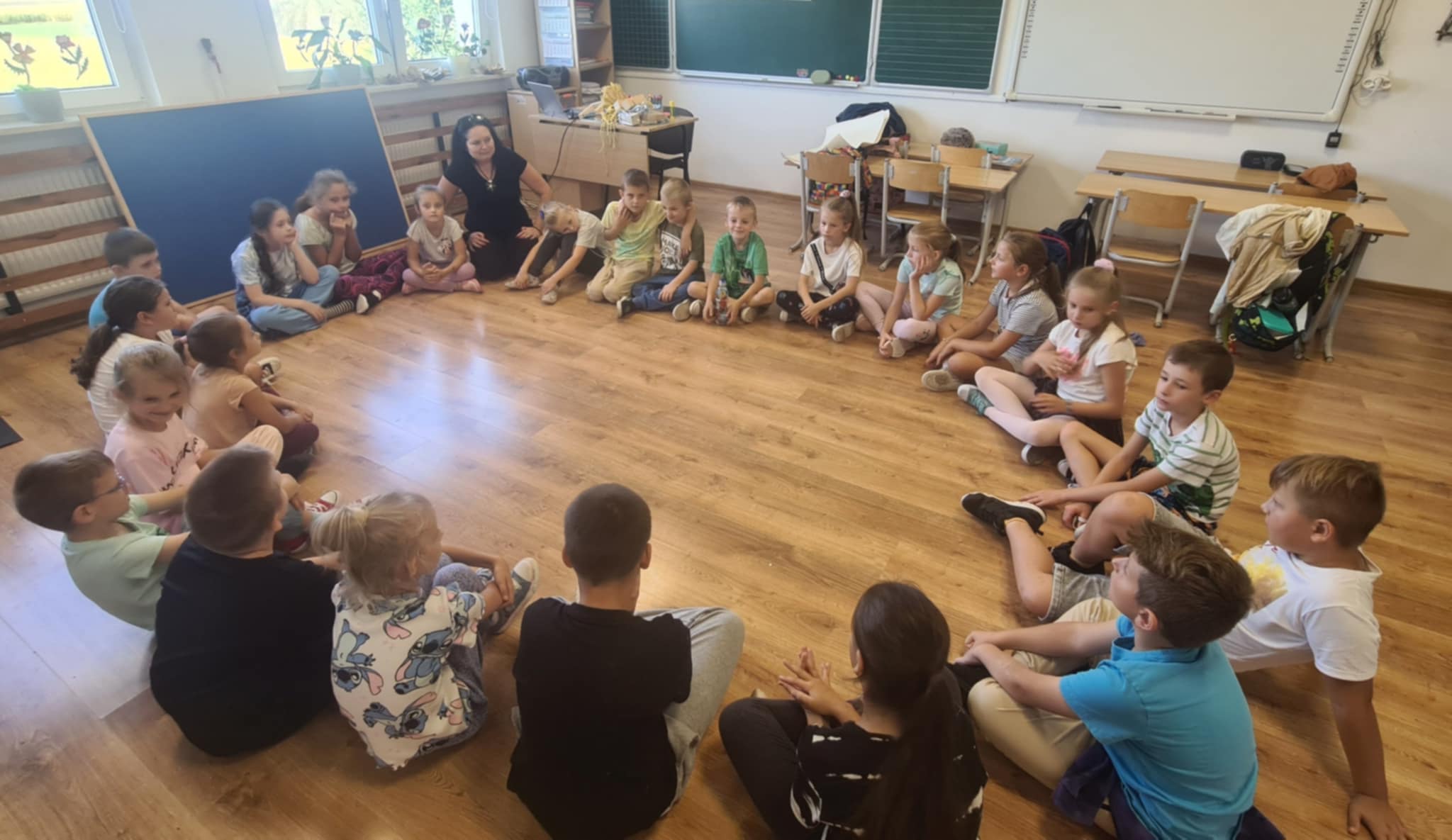 Uczniowie siedzą w kole i rozmawiają z prowadzącą zajęcia
