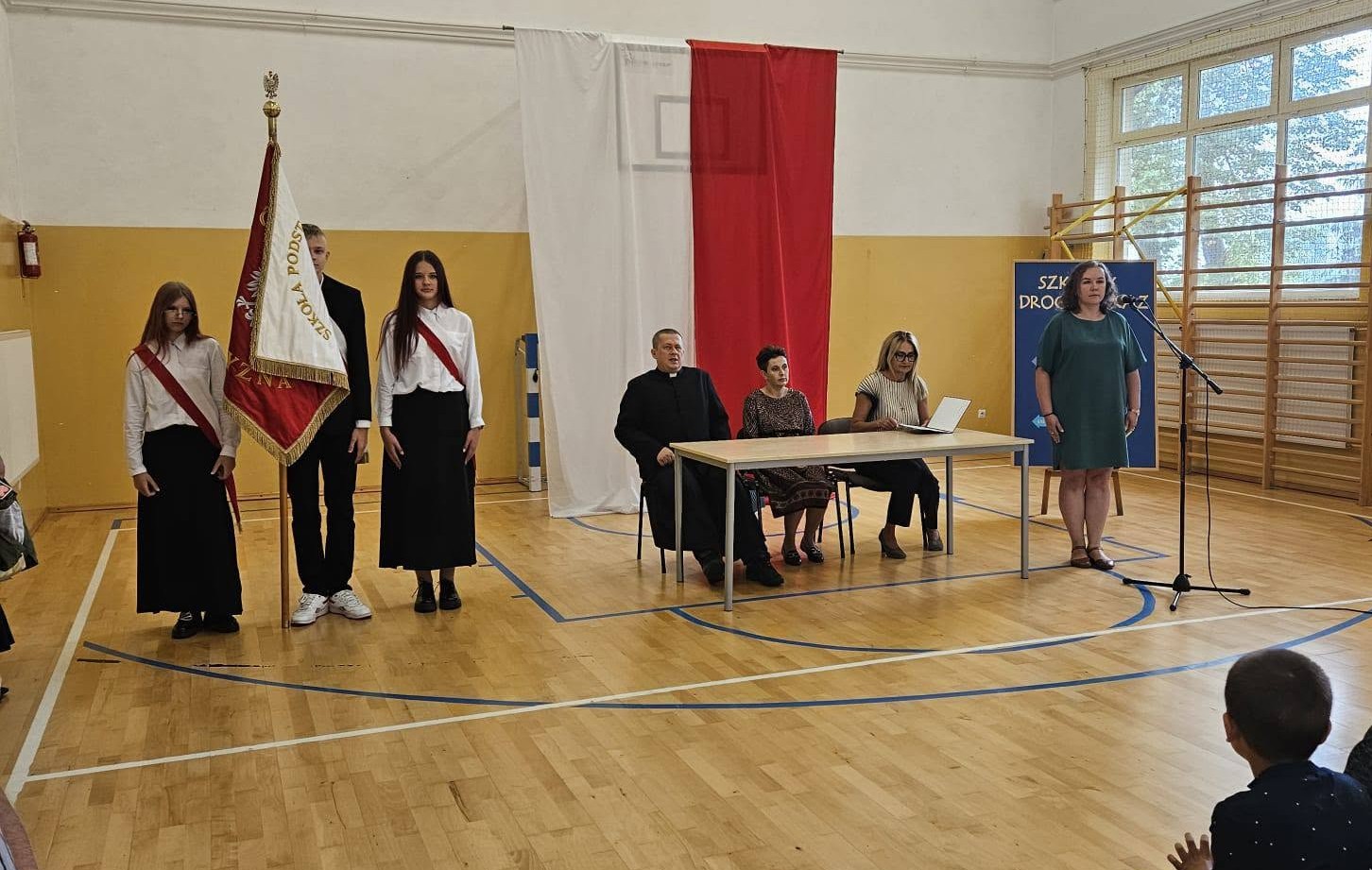Poczet sztandarowy oraz pani dyrektor z nauczycielami podczas uroczystości rozpoczęcia roku szkolnego