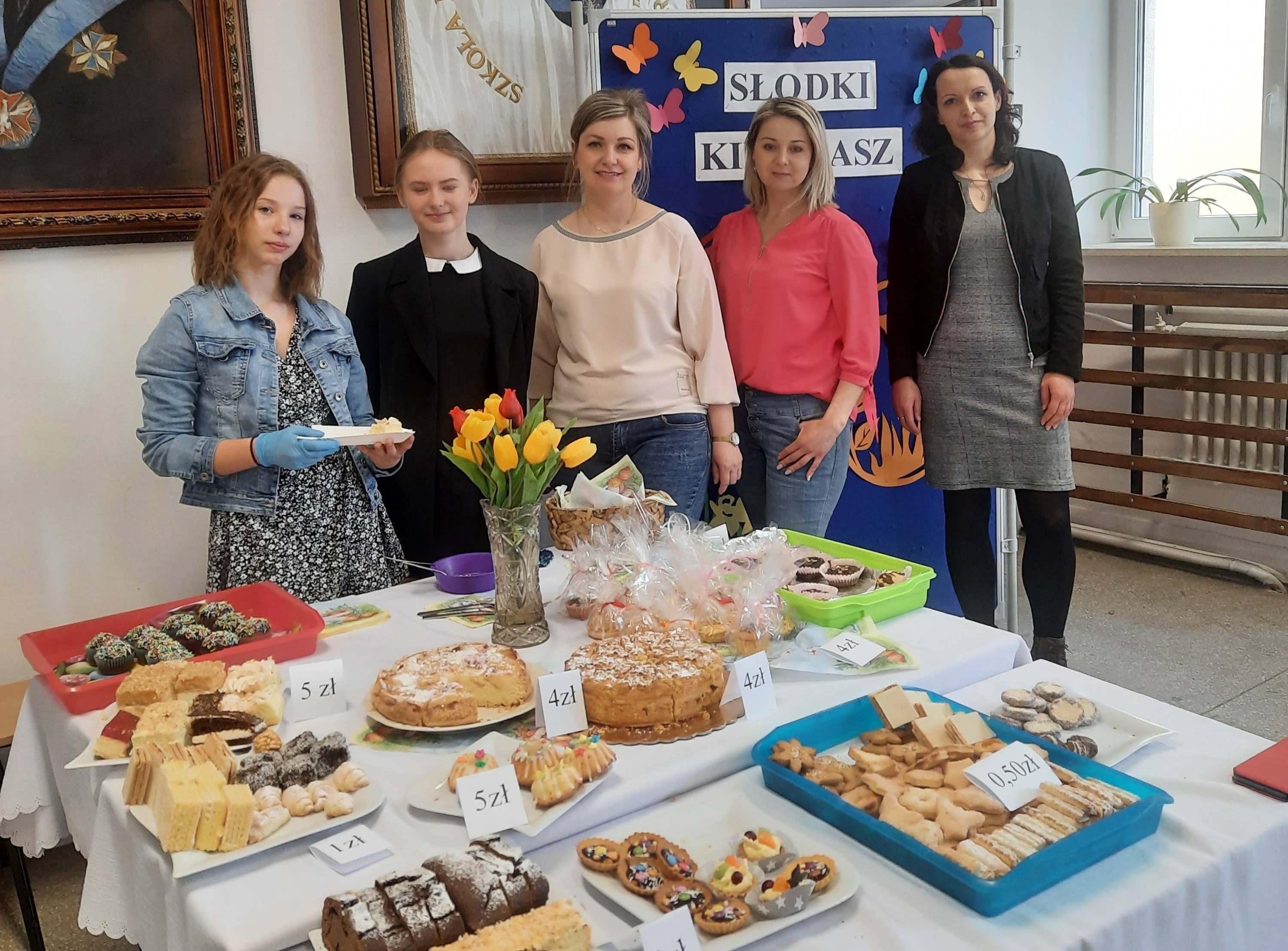 Trzy nauczycielki i dwie uczennice przy stole zastawionym talerzami z pokrojonym ciastem