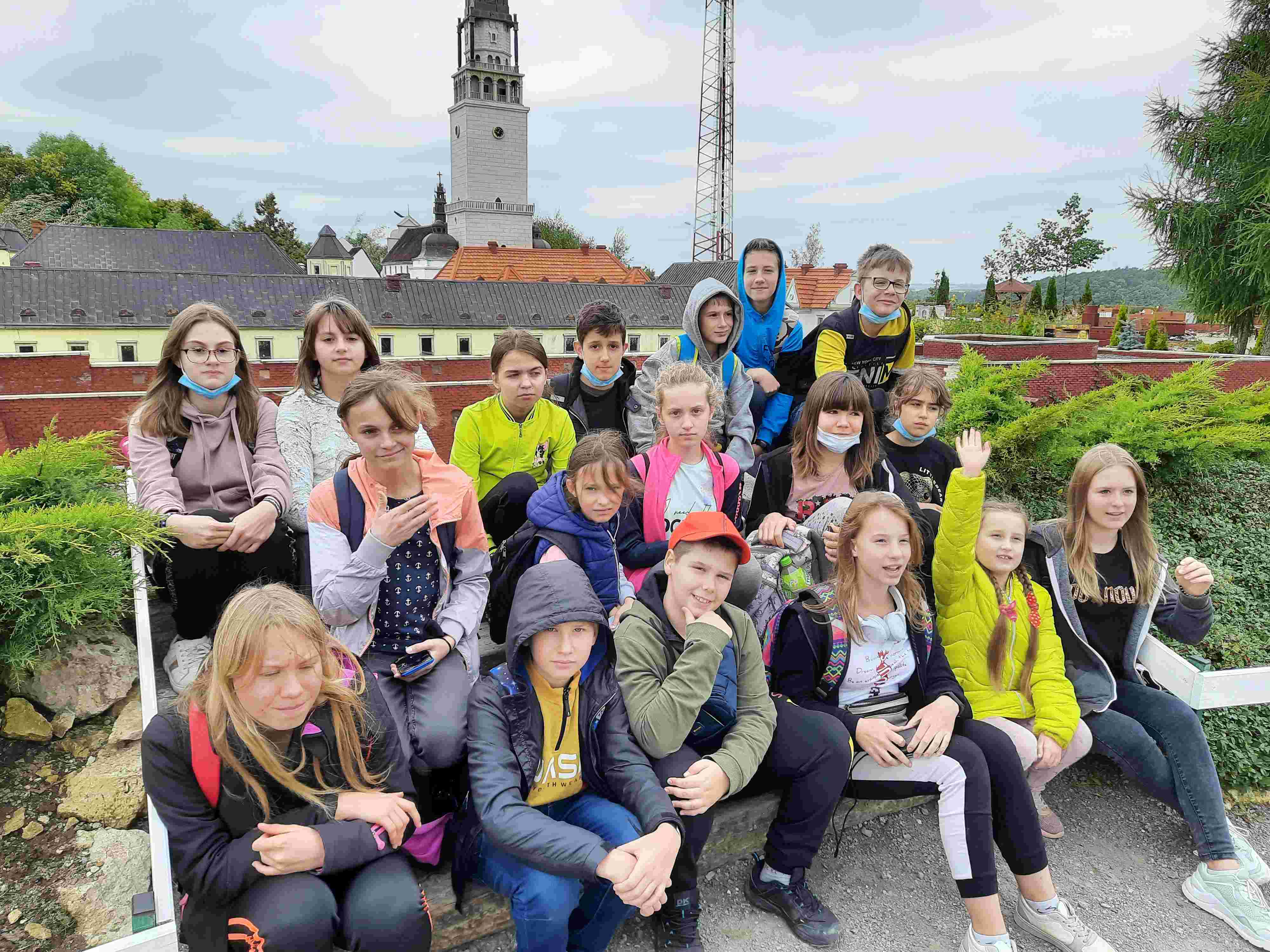 Uczniowie klas 6-8 siedzą na schodach. W tle park miniatur