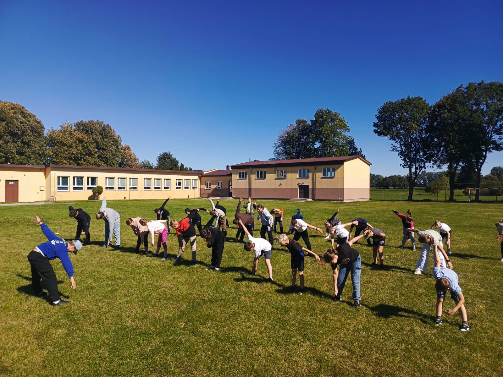 Uczniowie wykonują ćwiczenia rozciągające na świeżym powietrzu.