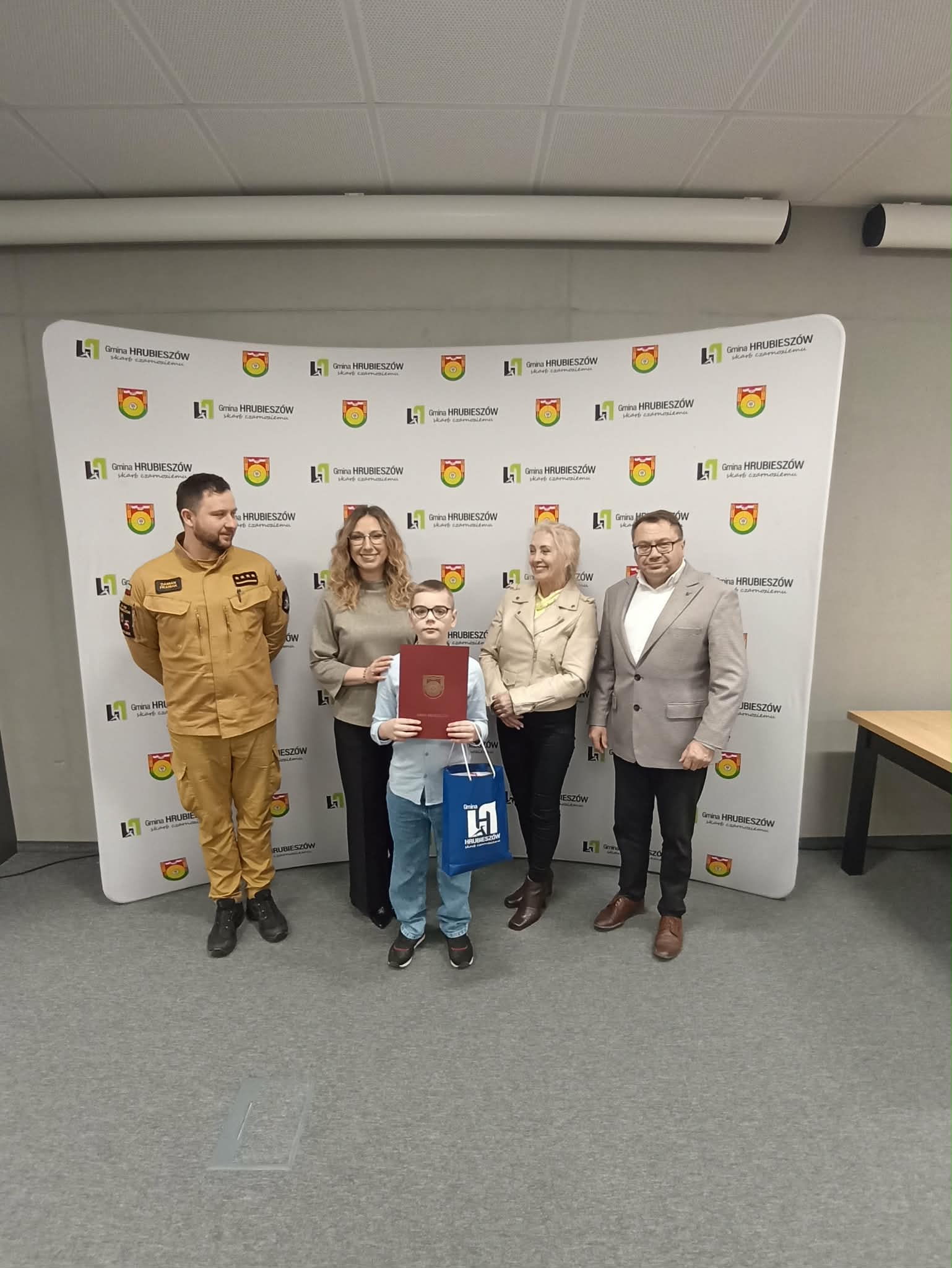 Uczestnicy gminnych eliminacji turnieju wiedzy pożarniczej stoją w grupie z dyplomami i nagrodami. Towarzyszą im organizatorzy oraz przedstawiciel straży pożarnej.