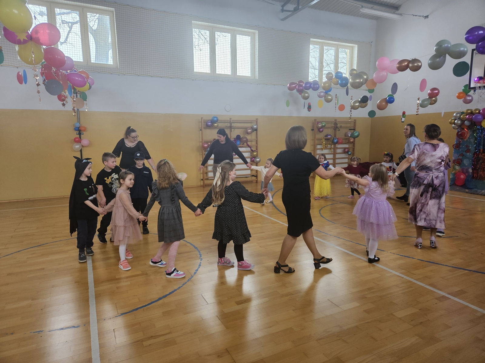 Uczniowie i nauczyciele tańczący w rytmie muzyki na udekorowanej sali gimnastycznej