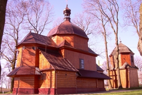 Drewniany budynek z dachem w kształcie kopuły, W oddali drugi budynek drewniany, drzewa bez liści