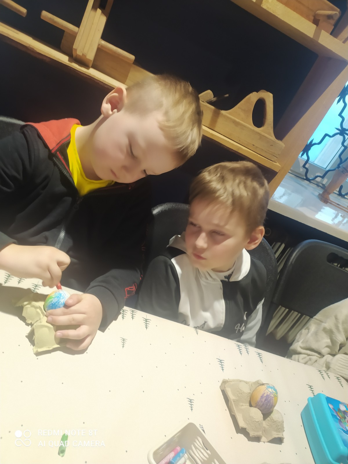 Chłopcy własnoręcznie dekorują pisankę wielkanocną.