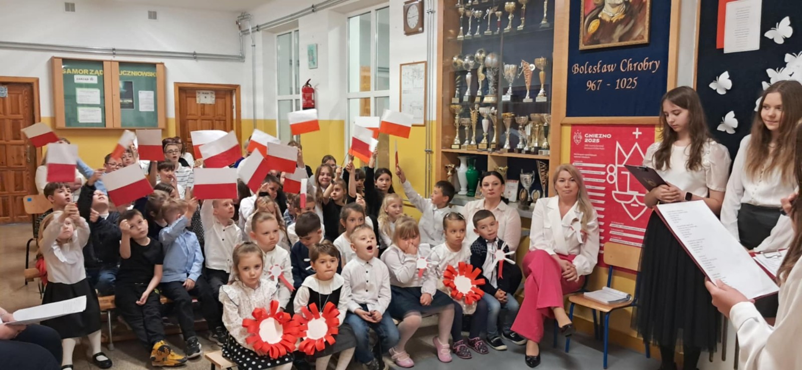 Dzieci wraz z uczniami szkoły podstawowej oraz nauczycielkami wysłuchują przygotowanej akademii.