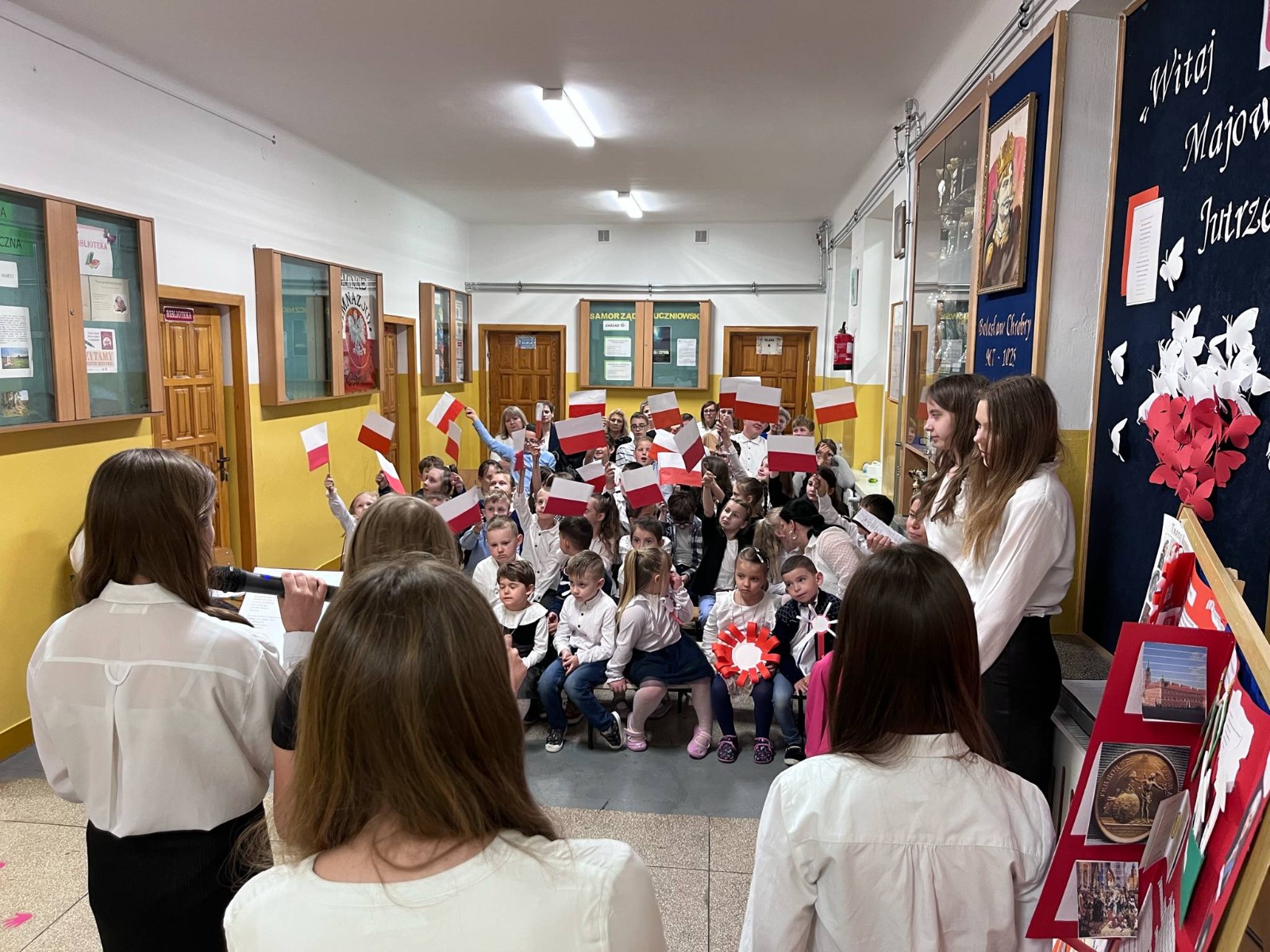Dzieci wraz z uczniami szkoły podstawowej oraz nauczycielkami wysłuchują przygotowanej akademii.
