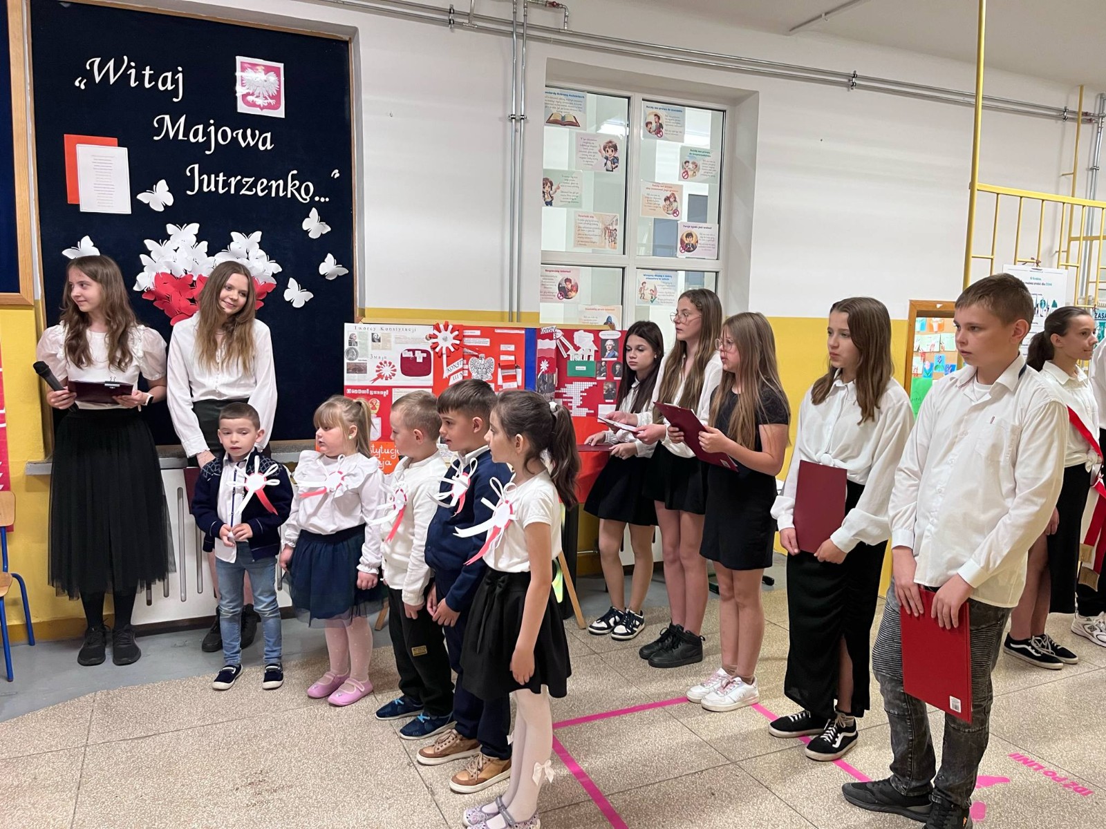 Uczniowie szkoły podstawowej wraz z dziećmi z oddziału przedszkolnego biorą udział w akademii z okazji świąt majowych
