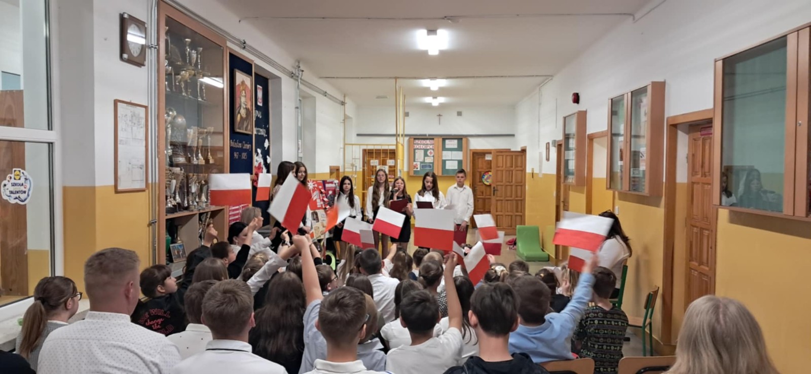 Dzieci wraz z uczniami szkoły podstawowej oraz nauczycielkami wysłuchują przygotowanej akademii.