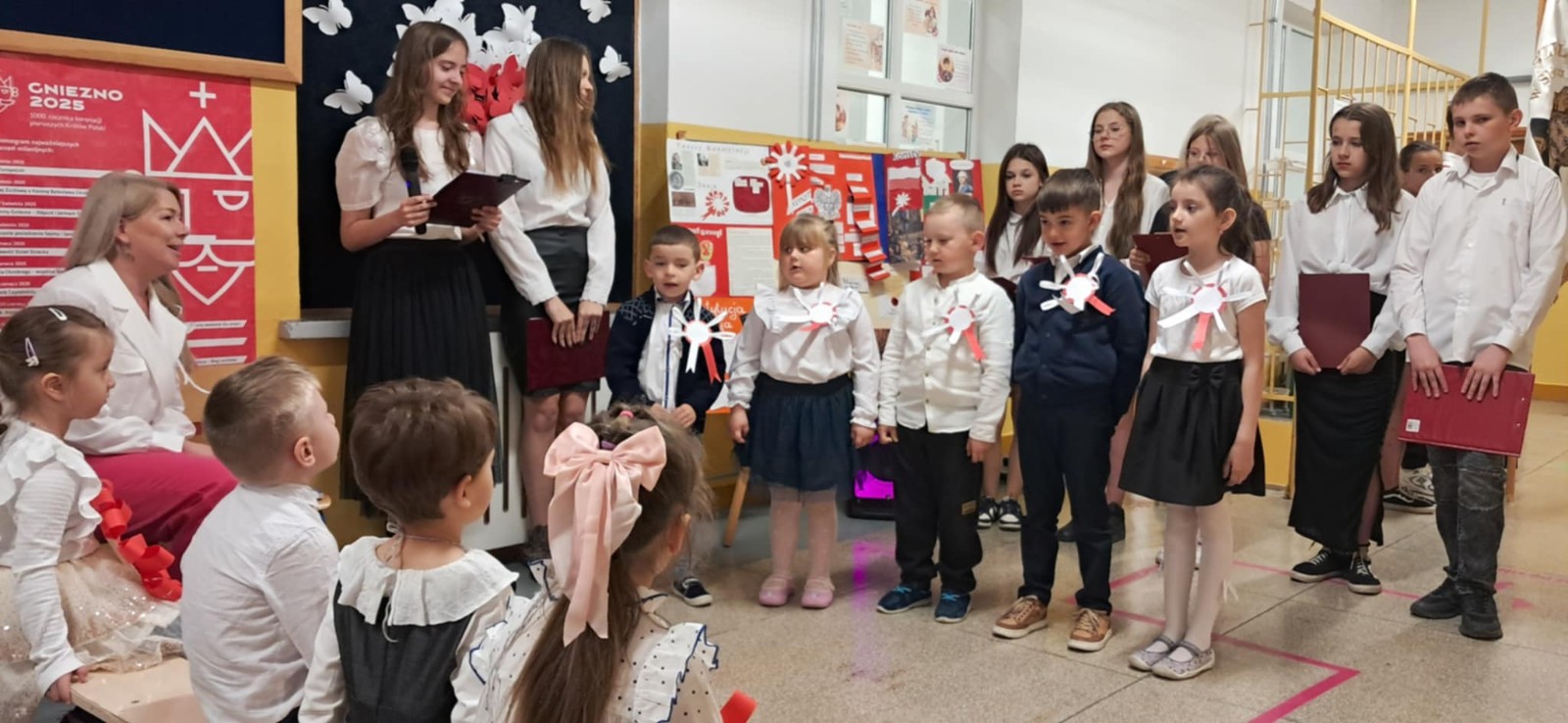 Uczniowie szkoły podstawowej wraz z dziećmi z oddziału przedszkolnego biorą udział w akademii z okazji świąt majowych
