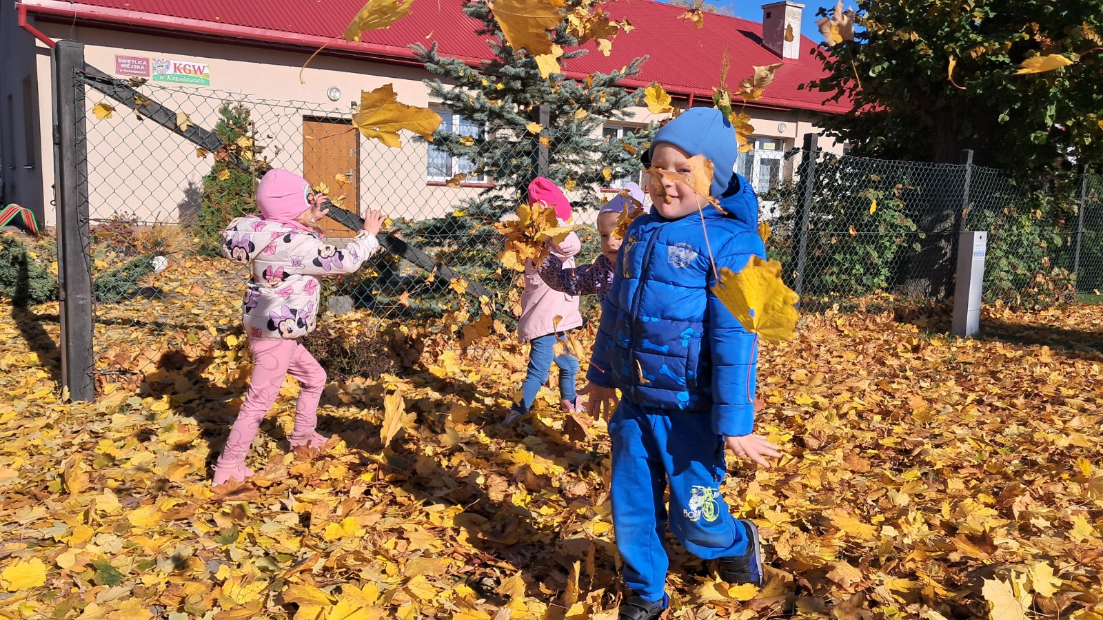 Dzieci prezentują się w tle jesiennych liści.