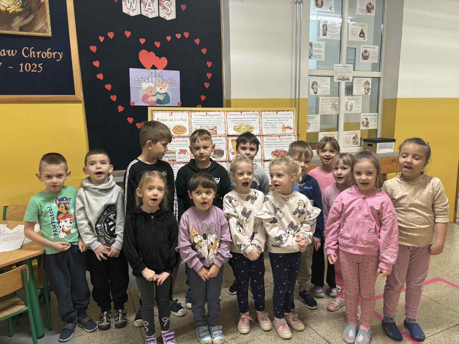 Dzieci pozują do pamiątkowego zdjęcia z różnymi ciekawostkami na temat pizzy.