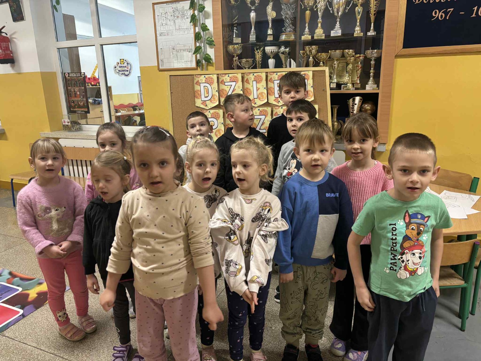 Dzieci pozują do zdjęcia na tle napisu dzień pizzy.