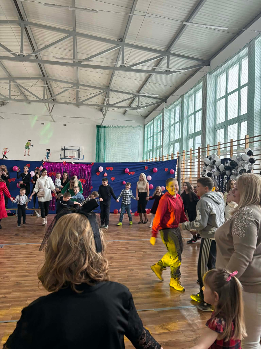 Dzieci wraz z uczniami biorą udział w zabawie choinkowej przy muzyce, a w środku tańczy biały miś.