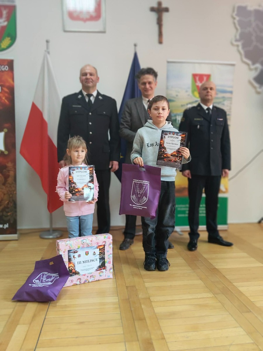 Dziecko prezentuje się z dyplomem i nagrodą w konkursie pożarniczym.