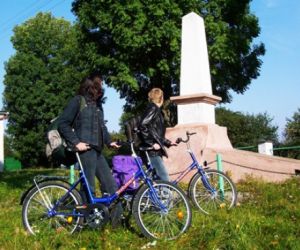 Dwie osoby z rowerami stojące przy białym monumencie 