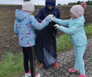 Dwie dziewczynki i chłopiec wrzucają zebrane śmieci do worka