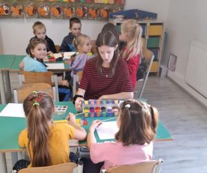 Zabawy integracyjne dla najmłodszych – uczennica klasy siódmej maluje farbami z sześciolatkami