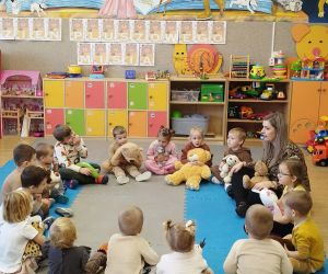 Przedszkolaki siedzą w kole i rozmawiają z wychowawczynią o przyniesionych misiach