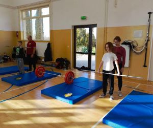 Uczeń i uczennica podnoszą sztangi pod opieką trenerów