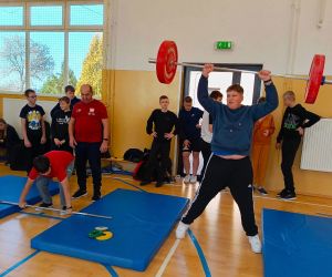 Jeden uczeń podnosi sztangę z obciążeniem, a drugi odkłada swoją sztangę na materace