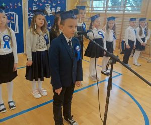 Uczeń klasy pierwszej przy mikrofonie, w tle pozostali pierwszoklasiści