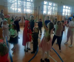Uczniowie klas młodszych i przedszkolaki w kolorowych strojach tańczą w grupie