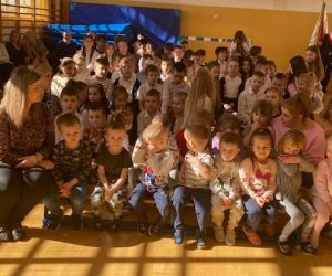 Dzieci z nauczycielami siedzą na ławkach