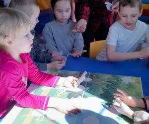 Na zdjęciu widoczne są dzieci siedzące przy stoliku.