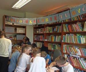 Na zdjęciu widoczne są dzieci w otoczeniu regałów z książkami.