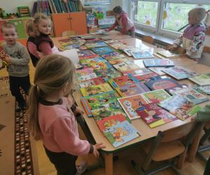 Na zdjęciu widoczne są dzieci przeglądające rozłożone na stole książki. 