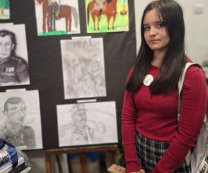 Uczennica na tle tablic ze zwycięskimi pracami