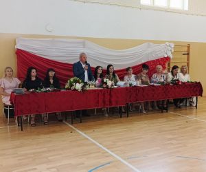 Dyrektor przemawia podczas uroczystości szkolnej a nauczyciele siedzą obok niego.