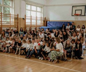 Uczniowie z rodzicami siedzą na ławkach