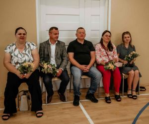 Rodzice ósmoklasistów siedzą na krzesłach przy ścianie