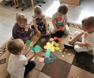 Kilkoro dzieci siedzi na dywanie i sortuje papierowe kółka według kolorów.