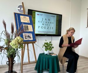 Pani Dyrektor czyta poezję, siedząc na tle dekoracji okolicznościowej