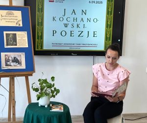Nauczycielka języka polskiego czyta poezję, siedząc na tle dekoracji okolicznościowej