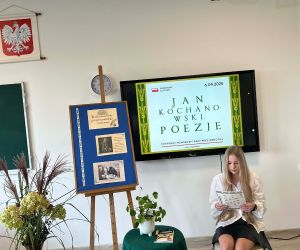 Uczennica klasy VII czyta poezję, siedząc na tle dekoracji okolicznościowej