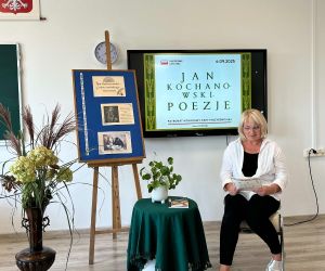 Nauczycielka muzyki czyta poezję, siedząc na tle dekoracji okolicznościowej