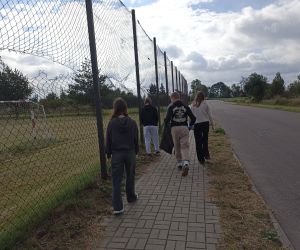 Grupa uczniów zbiera śmieci przy szosie.