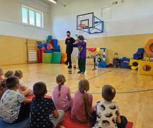 Klaun Walduś żongluje piłeczkami, obok niego stoi uczeń biorący udział w pokazie.