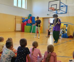 Klaun Walduś wspólnie z asystentem pokazuje uczniom sztuczkę z wykorzystaniem rekwizytów.