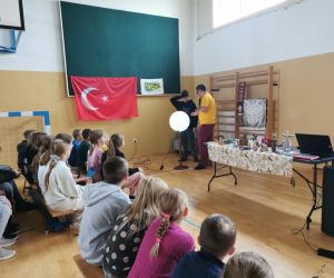 Podróżnik wraz z uczniem pokazują globus. Na stole widoczne są tureckie pamiątki i figurki.
