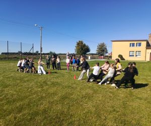 Starsi uczniowie rywalizują w przeciąganiu liny na boisku szkolnym.
